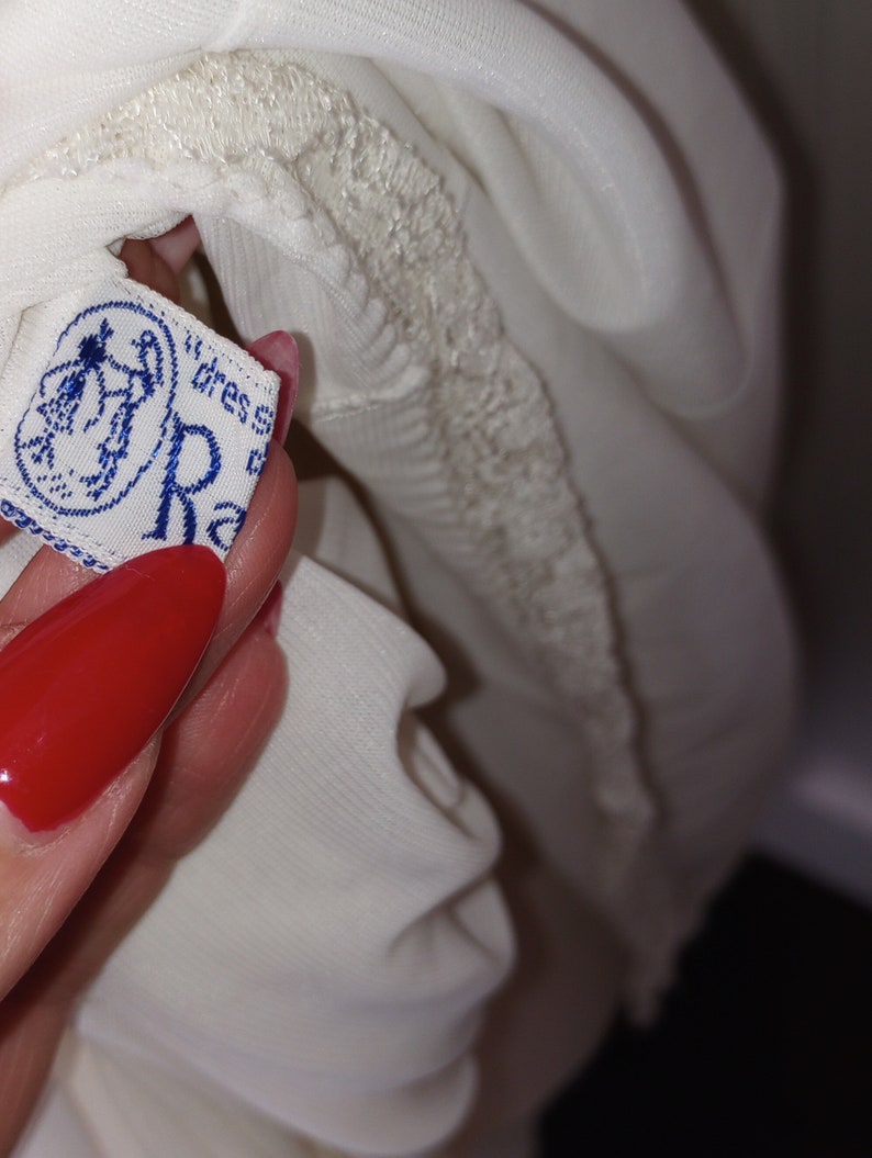May include: White lace trim on a white garment with a blue and white label that reads "dress size R"