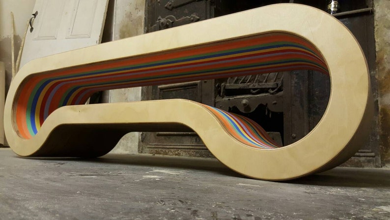 May include: A wooden bench with a rainbow-colored stripe design. The bench is curved and has a unique shape.