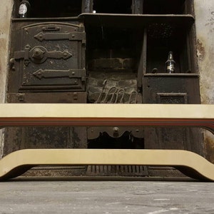 May include: A light wood bench with a curved design and a rainbow stripe detail. The bench is in front of a vintage fireplace.