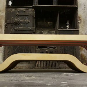 May include: A curved, multi-colored wooden bench with a rainbow design. The bench is made of plywood and has a unique, modern design.