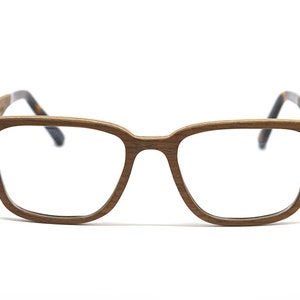 K&ouml;nnte beinhalten: Brille mit einem rechteckigen Rahmen in brauner Holzmaserung. Die B&uuml;gel sind d&uuml;nn und gerade und gehen an den Enden in ein dunkles Schildpattmuster &uuml;ber. Der Steg ist gerade und verbindet die beiden breiten &Ouml;ffnungen f&uuml;r die Gl&auml;ser.