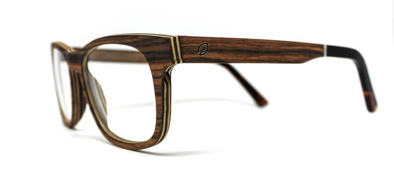 May include: Eyeglasses featuring a frame with a layered wood grain pattern in shades of brown and tan. The temples display a small circular logo with a leaf icon. The temple tips are black, and the frame includes clear lenses for vision correction.