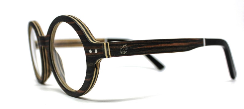 May include: Round eyeglasses featuring a dark brown and tan striped wood-grain frame. The temples are dark brown with a small circular logo emblem near the hinge. The frame front is constructed from layered wood with two silver rivets on each side.