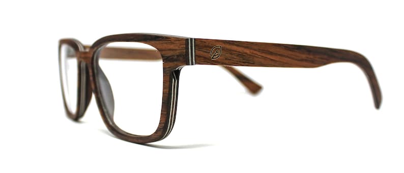 K&ouml;nnte beinhalten: Brille mit einem dunkelbraunen Holzmaserungsrahmen, der eine geschichtete Konstruktion mit sichtbaren hellen Streifen an den Kanten aufweist. Der Brillenb&uuml;gel zeigt ein kleines metallisches blattf&ouml;rmiges Logo-Emblem nahe dem Scharnier.