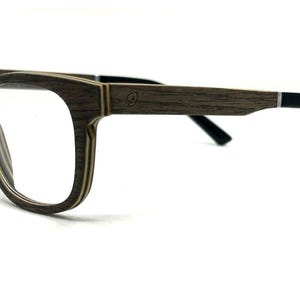 May include: Eyeglasses with a layered wood-grain frame featuring a dark brown and tan striped pattern. The temples are made of the same wood material, transitioning to solid black tips. A small leaf icon is engraved on the outer temple.