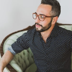 May include: A pair of brown-rimmed eyeglasses with a rectangular frame shape. The glasses feature a warm, wood-toned finish on the rims and temples, providing a distinct contrast against the face. The design is simple, functional, and classic.