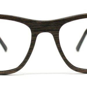 May include: Eyeglasses with a dark brown wood grain frame and clear lenses. The frame features a rectangular shape with rounded edges and thin black temple arms that connect to the wooden front with a small silver-colored metal hinge detail.