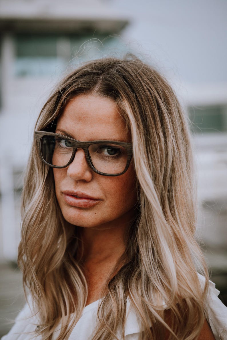 May include: Rectangular eyeglasses featuring a dark brown wood grain frame with a matte finish. The glasses have a thick bridge and wide temples, showcasing a natural textured wood pattern throughout the entire frame structure and dark lenses.