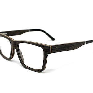May include: Spectacles with a dark brown, wood-grain textured frame and rectangular lenses. The temples feature a small engraved logo near the hinge and transition into solid black tips. The frame construction shows visible layered wood detailing.