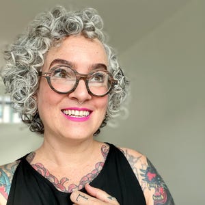May include: Round eyeglasses featuring a dark brown and black wood-grain textured frame. The glasses have a circular shape with a visible horizontal striped pattern on the rims and small silver-toned metal accents on the outer corners of the frame.
