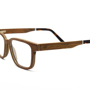 K&ouml;nnte beinhalten: Brille mit einem geschichteten Holzrahmen mit sichtbarer Maserung. Die B&uuml;gel bestehen aus Holz und gehen an den Enden in ein Schildpattmuster &uuml;ber. Ein kleines kreisf&ouml;rmiges Logo ist an der Au&szlig;enseite des B&uuml;gels eingraviert.