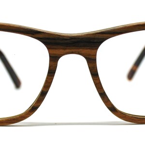 May include: Eyeglasses featuring a frame with a distinct brown and black wood grain pattern. The glasses have a classic rectangular shape with a bridge and two temples that extend backward, showing a dark interior finish on the temple arms.