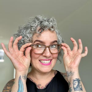 K&ouml;nnte beinhalten: Brille mit rechteckigem Rahmen in braun-beigem Holzmaserungsmuster. Die Brille hat klare Gl&auml;ser und einen Steg, der die beiden R&auml;nder verbindet. Der Rahmen ist durchgehend mit einer horizontalen, gestreiften Textur versehen.