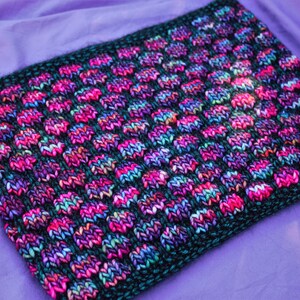 May include: A close-up of a knitted fabric with a black background and a pattern of colorful dots. The fabric is soft and textured, and the colors are vibrant and eye-catching.