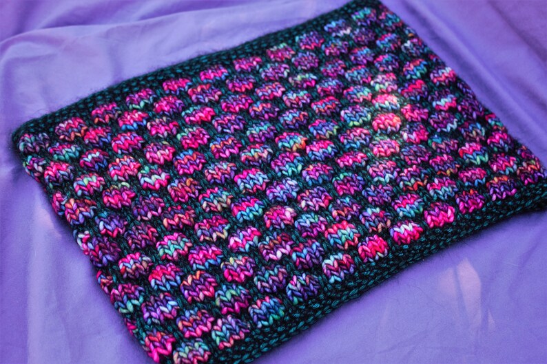 May include: A close-up of a knitted fabric with a black background and a pattern of colorful dots. The fabric is soft and textured, and the colors are vibrant and eye-catching.