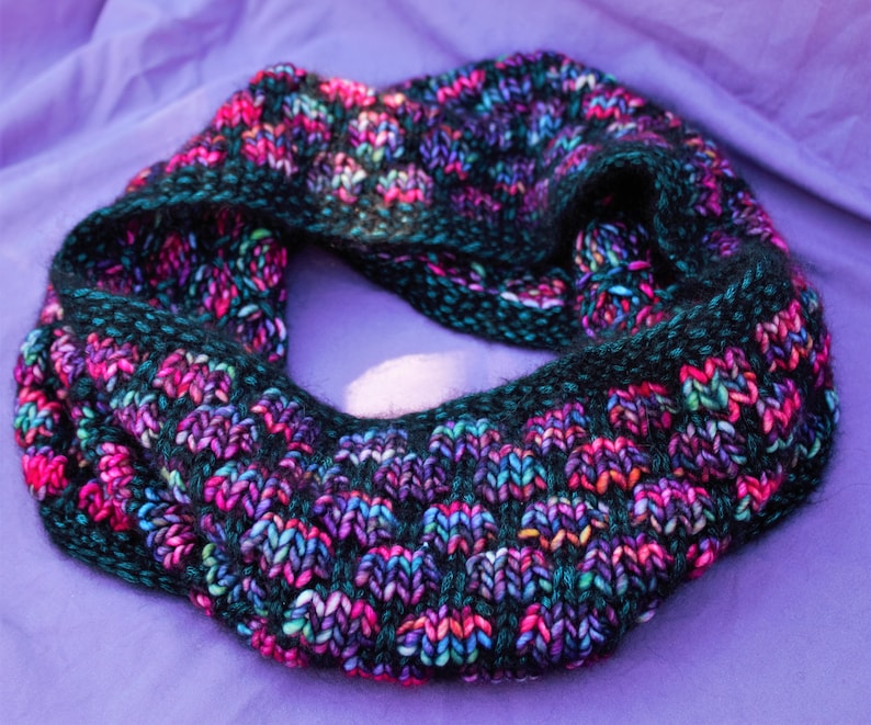 May include: A black, purple, and teal knitted infinity scarf with a textured pattern.