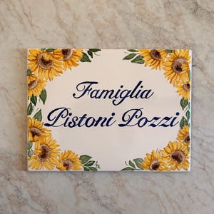 Handbeschilderd huisnummerbord met zonnebloemmotief, huisnummer en namen op Italiaanse keramische tegel, een gepersonaliseerd cadeau voor de familie.