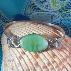 May include: A silver bangle bracelet with a green and white glass oval bead. The bead has a marbled effect.