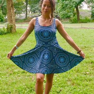 May include: A sleeveless, flared dress with a geometric starburst pattern in shades of blue and white. The dress is worn with blue high-top sneakers. The person is standing on green grass in a park setting.
