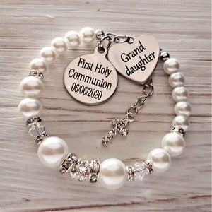 May include: A white pearl bracelet with a silver charm that says "First Holy Communion 06/06/2020" and a silver heart charm that says "Grand daughter".