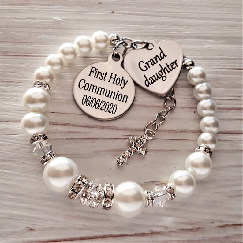 May include: A white pearl bracelet with a silver charm that says "First Holy Communion 06/06/2020" and a silver heart charm that says "Grand daughter".