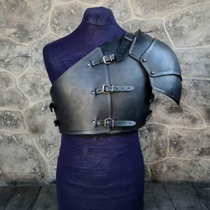 May include: Black leather shoulder armor with buckles and straps. The armor is on a mannequin with a purple fabric base.