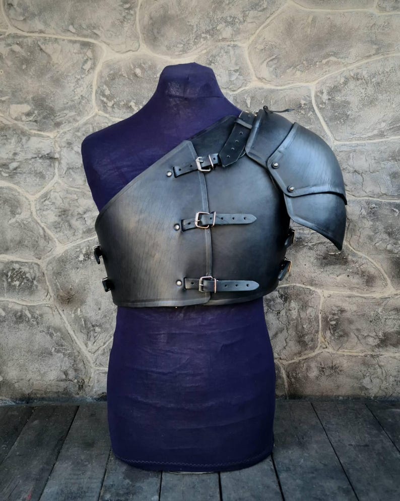 May include: Black leather shoulder armor with buckles and straps. The armor is on a mannequin with a purple fabric base.