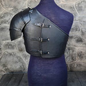 May include: Black leather armor with a metal shoulder piece. The armor has straps and buckles.