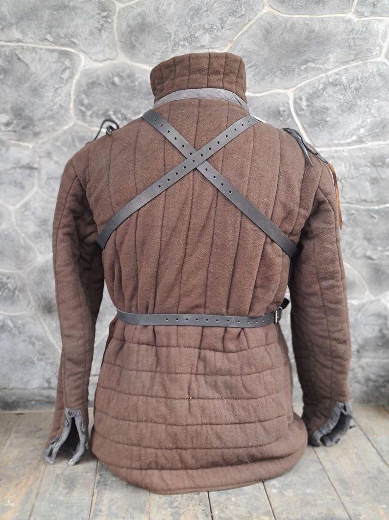 May include: A brown quilted jacket with a black leather strap across the back and a black leather belt around the waist.
