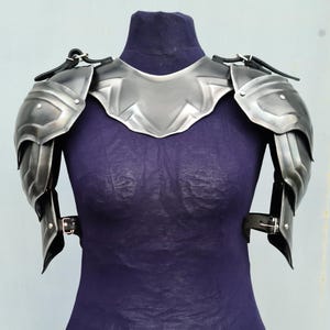 You can see blackened version of the pair of shoulders with gorget. The shoulders made from steel and protect your arm from neck to elbow. The shoulders have an ornament all over the entire surface of the metal.