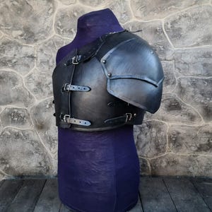 May include: Black leather armor with a shoulder piece and straps. The armor is on a purple mannequin.