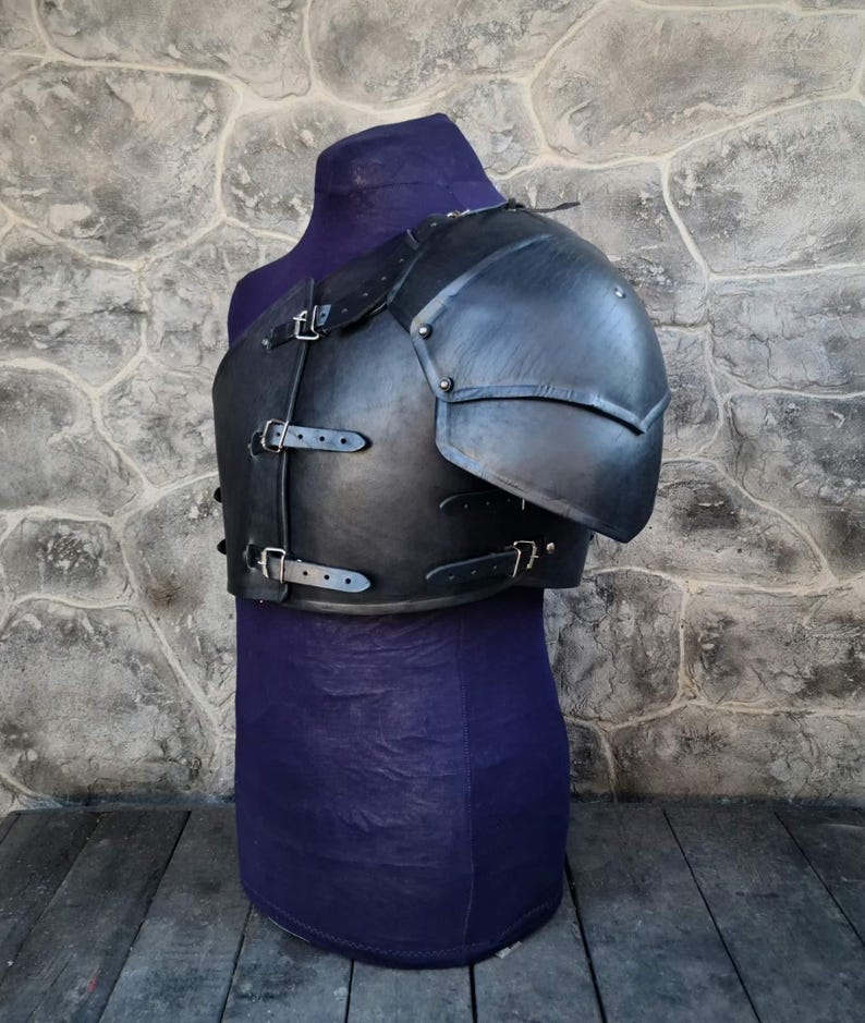 May include: Black leather armor with a shoulder piece and straps. The armor is on a purple mannequin.