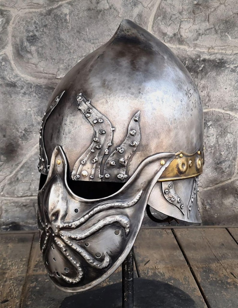 May include: A silver-colored metal helmet with an octopus design on the face guard and side. The helmet has a pointed top and a gold-colored band around the base. The octopus design features tentacles and suction cups.
