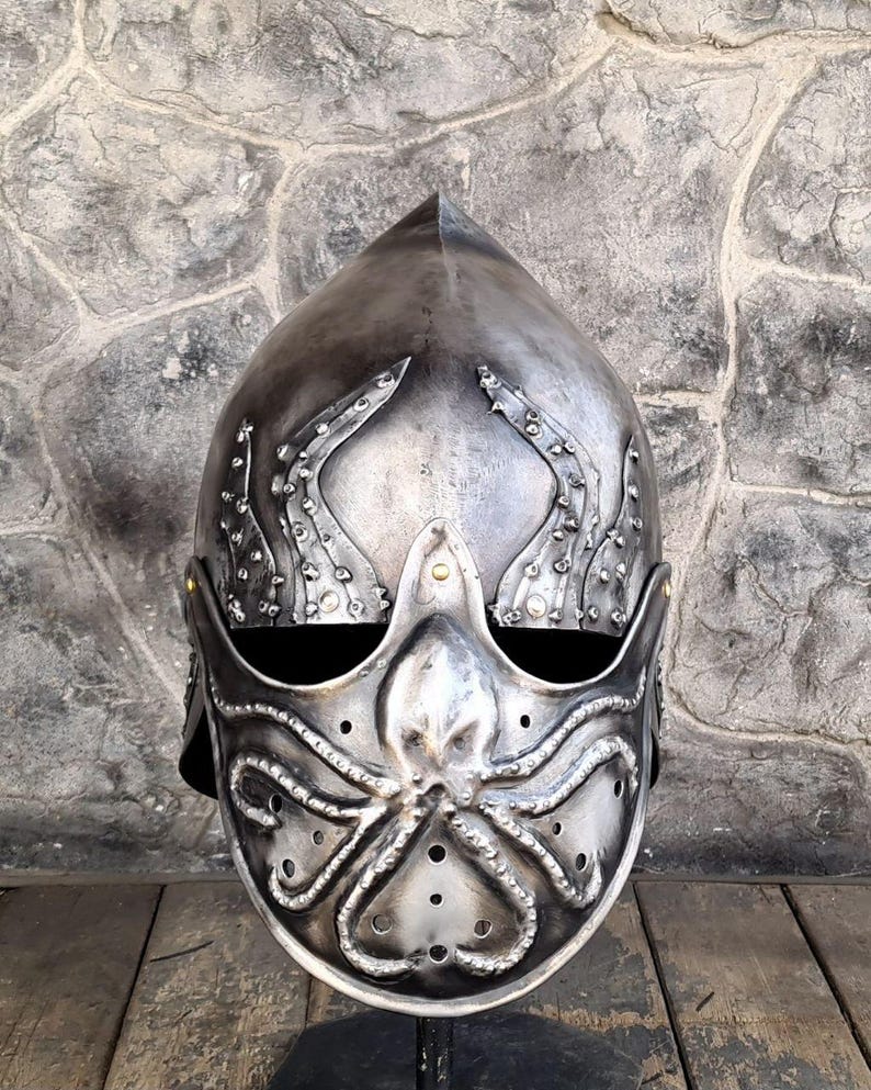May include: A silver-colored helmet with an octopus design on the face and tentacles extending up the sides. The helmet has a pointed top and small rivets. The design is detailed and appears to be made of metal.