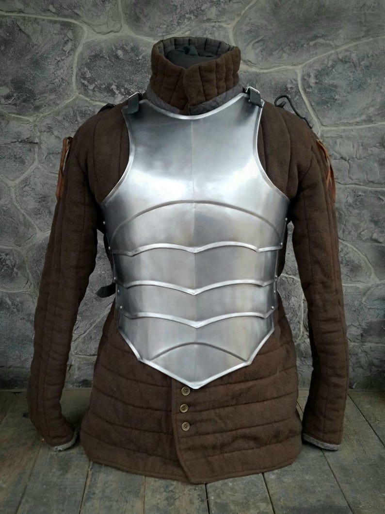 May include: A silver-colored metal breastplate with a decorative design. The breastplate is worn over a brown quilted jacket.