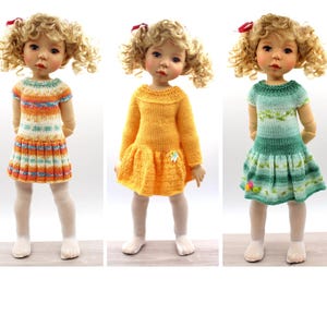 Peut inclure: Trois poupées aux cheveux blonds bouclés et nœuds rouges, portant chacune une robe tricotée différente. La première porte une robe rayée multicolore à manches courtes, la deuxième une robe jaune unie à manches longues et la troisième une robe verte dégradée.