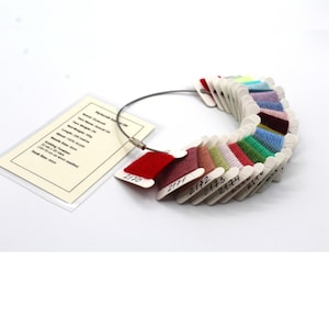 May include: A yarn color swatch ring with a variety of yarn colors, including red, pink, green, blue, and purple. Each swatch is labeled with a number. A tag with text is attached to the ring.