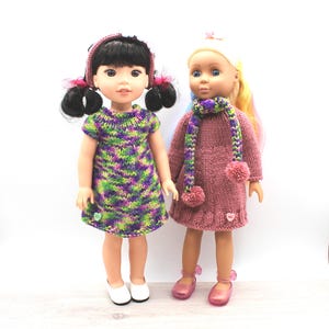 Pode incluir: Duas bonecas vestidas com roupas de malha feitas à mão. Uma boneca está com um vestido verde, roxo e branco com sapatos brancos. A outra boneca está com um vestido rosa com um cachecol a condizer e sapatos rosa. Ambas as bonecas têm acessórios.