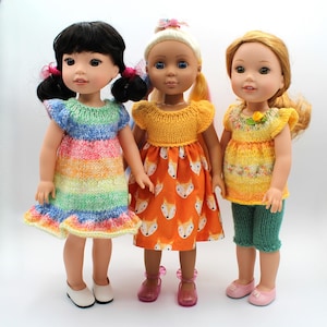 Pode incluir: Três bonecas vestidas com roupas coloridas. Uma boneca usa um vestido listrado arco-íris, outra uma blusa amarela e uma saia laranja com estampa de raposa, e a terceira uma blusa amarela e shorts verdes. Cada boneca tem sapatos.