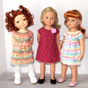 May include: Three dolls wearing different knitted dresses. The doll on the left is wearing a pink and brown striped dress with floral embellishments and white boots. The middle doll is wearing a burgundy dress with a single pink flower embellishment and black shoes. The doll on the right is wearing a rainbow striped dress with white flower embellishments and pink shoes.
