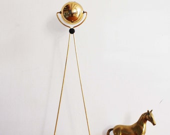May include: A gold-toned table lamp with a spherical shade and a tripod base. The lamp is on a wooden surface next to a gold-toned horse figurine.