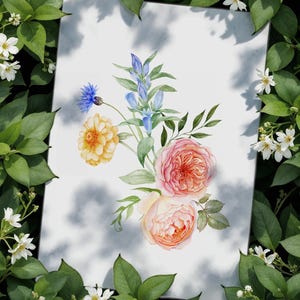 Op de afbeelding: Aquarel bloemenkunst print met een boeket rozen, blauwe klokjes en andere bloemen in roze, geel en blauw. Het kunstwerk staat tegen een witte achtergrond met een schaduweffect, omringd door groene bladeren en witte bloemen.