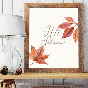 May include: A printable art print with a watercolor illustration of autumn leaves in shades of red and orange. The text "Hello Autumn!" is written in cursive script.