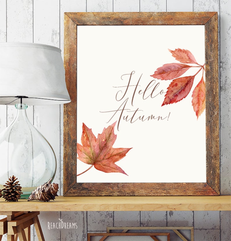 May include: A printable art print with a watercolor illustration of autumn leaves in shades of red and orange. The text "Hello Autumn!" is written in cursive script.