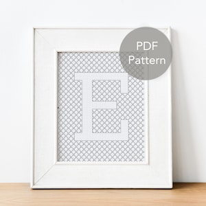 Könnte beinhalten: Ein weißer Rahmen mit einem schwarz-weißen Kreuzstichmuster des Buchstabens "E" im Inneren. Der Rahmen hat einen weißen Passepartout und einen grauen Kreis mit dem Text "PDF Pattern" in Schwarz.