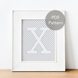 Peut inclure: Un cadre blanc avec un motif de point de croix noir et blanc de la lettre "X" à l'intérieur. Le cadre est sur une surface en bois. Le texte "PDF Pattern" est dans un cercle gris sur le côté droit de l'image.