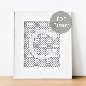 Op de afbeelding: Een wit frame met een zwart-wit kruissteekpatroon van de letter C. Het frame heeft een witte passe-partout en een label met de tekst "PDF-patroon".