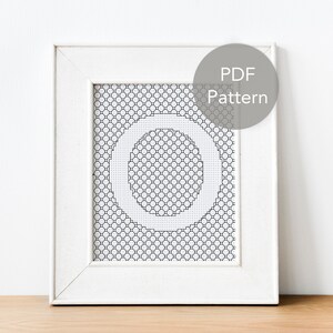 May include: A white frame with a black and white cross-stitch pattern of the letter "O" inside. The frame has a white mat and a label that says "PDF Pattern".