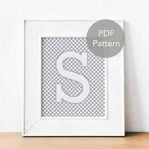 Könnte beinhalten: Ein weißer Rahmen mit einem schwarz-weißen Kreuzstichmuster des Buchstabens "S" im Inneren. Der Rahmen hat einen weißen Passepartout und einen weißen Hintergrund. Der Text "PDF Pattern" befindet sich in einem grauen Kreis in der oberen rechten Ecke des Bildes.