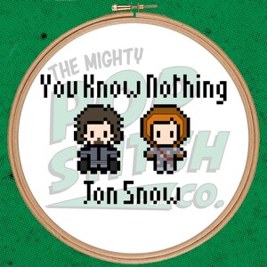 May include: A white embroidery hoop with a brown wooden frame. The hoop features a pixelated image of two characters from the TV show Game of Thrones, Jon Snow and Ygritte. The text "The Mighty Pop Stitch Co." and "You Know Nothing Jon Snow" is printed on the hoop.